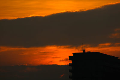 Low angle view of silhouette buildings against orange sky
