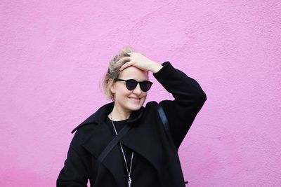 Woman with hand in hair wearing sunglasses while standing against pink wall