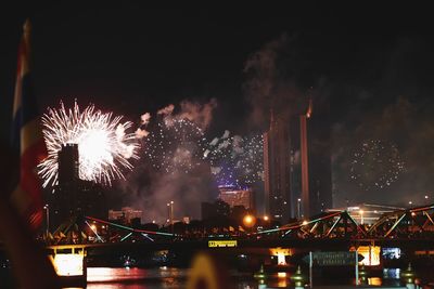 Firework display over river against sky in city at night