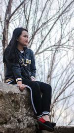 Full length of young woman sitting on bare tree