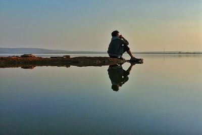 Man sitting at beach against sky during sunset