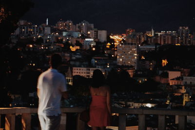 Rear view of people looking at illuminated buildings in city at night