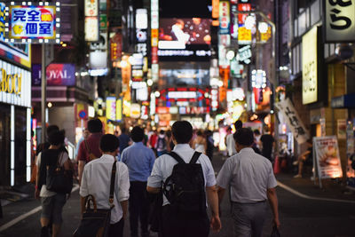 Rear view of people walking on city street at night