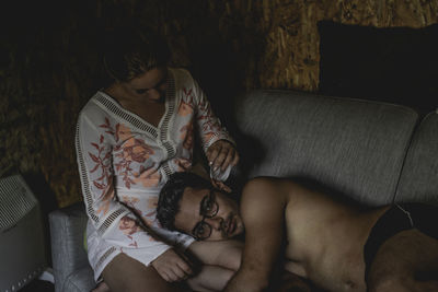 High angle portrait of shirtless young man lying on girlfriend lap at home