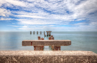 Scenic view of wooden posts in sea against sky