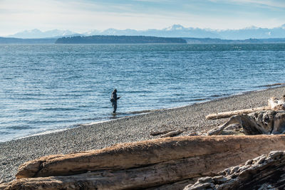 Man standing on rock by sea against sky