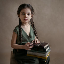 A girl with long pigtails sits and holds a stack of books in her lap