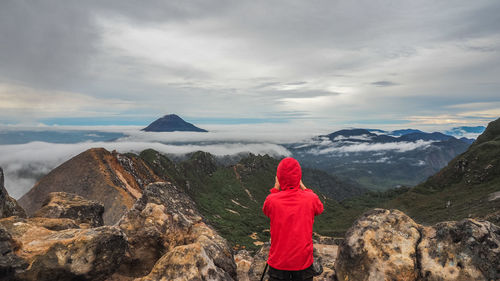 Rear view of woman standing on rock against sky