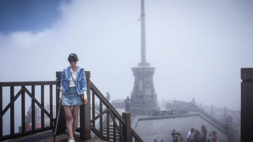 Smiling woman standing by railing during foggy weather