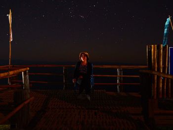 Full length of woman sitting on railing at night
