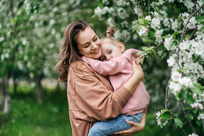 Young mother with her daughter in her arms in a blooming apple orchard