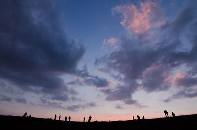 Silhouette people on land against sky during sunset