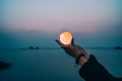 Man holding umbrella against sea during sunset