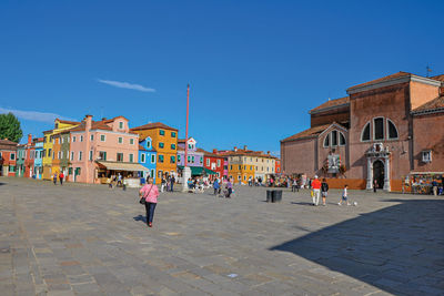 People on street amidst buildings in city against clear blue sky