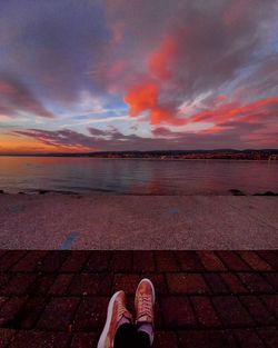 Low section of man on sea against sky during sunset