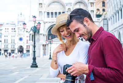 Happy young couple holding camera while standing in city