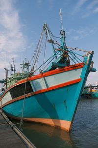 Fishing boat moored at harbor against sky