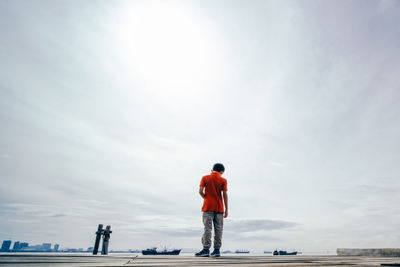 Rear view of boy standing at harbor against sky