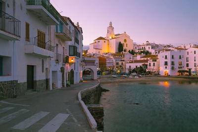 Illuminated buildings by road against sky in city at dusk