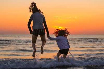 Full length of friends walking on beach against sky during sunset