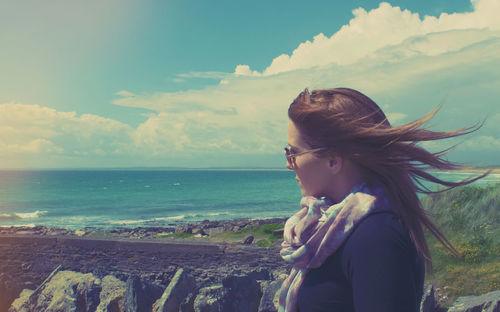 Woman wearing sunglasses against sea and cloudy sky on sunny day