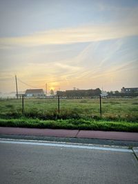 Road by field against sky during sunset