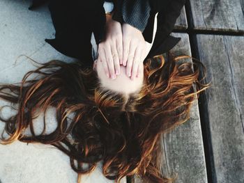 High angle view of woman covering face while lying on wooden floor