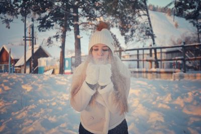 Young woman blowing snow while standing on field during winter