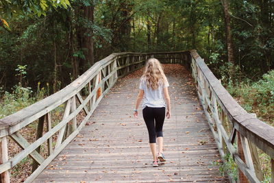 Rear view of woman walking on footbridge in forest