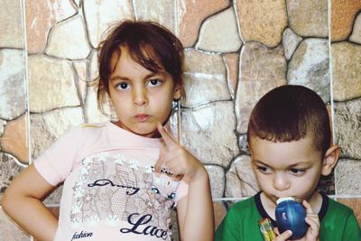 Portrait of girl with brother against wall