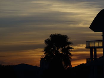 Silhouette tree by building against sky during sunset