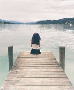 Rear view of woman sitting on pier over lake