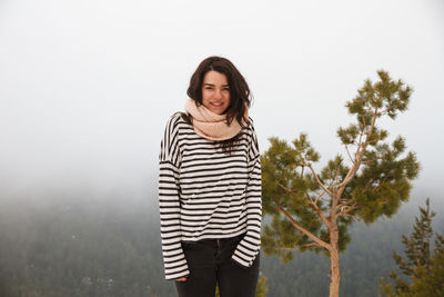 Smiling young woman standing against sky