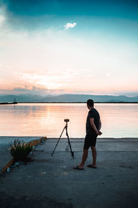 Man looking at view of lake while standing by camera during sunset