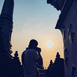 Rear view of silhouette man photographing against sky at sunset