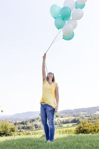 Full length of woman holding balloons against clear sky