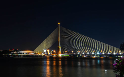 Illuminated bridge over river against sky at night