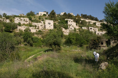 Rear view of men walking on grass against buildings and sky