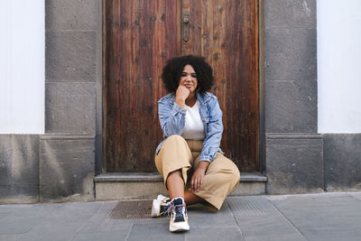 Young woman with hand on chin sitting in front of wooden door