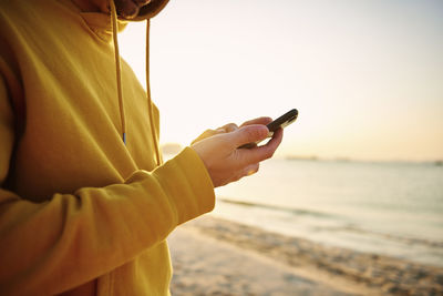 Midsection of man using smart phone against sky during sunset