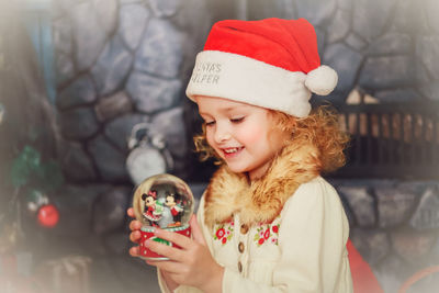 Cute smiling girl holding snow globe at home