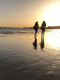 Silhouette people on beach against sky during sunset