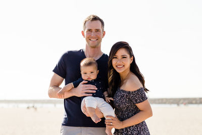 Mother & father holding young son & smiling on beach