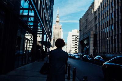 Rear view of man walking on street amidst buildings in city