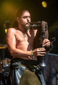 Low angle view of shirtless man playing bagpipe during concert