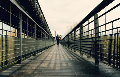 Rear view full length of woman walking on footbridge against sky