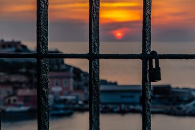 Close-up of metal fence against sunset sky