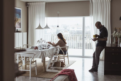 Female entrepreneur working while male colleague standing behind at home