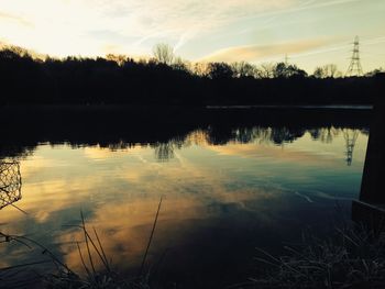 Reflection of silhouette trees in calm lake at sunset