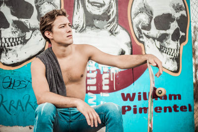 Full length of shirtless young man holding graffiti